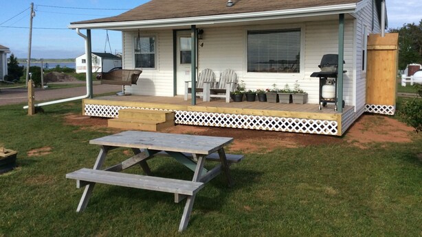 A single-story house with a porch, a grill, and a picnic table. - Schurmans Shore Cottage #4 (Summerside)