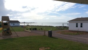 A grassy area with a playground, a picnic table, and a house with a white exterior. - Schurmans Shore Cottage #4 (Summerside)