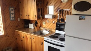 A compact kitchen with wooden cabinets, a stove, a sink, and a refrigerator. - Schurmans Shore Cottage #4 (Summerside)