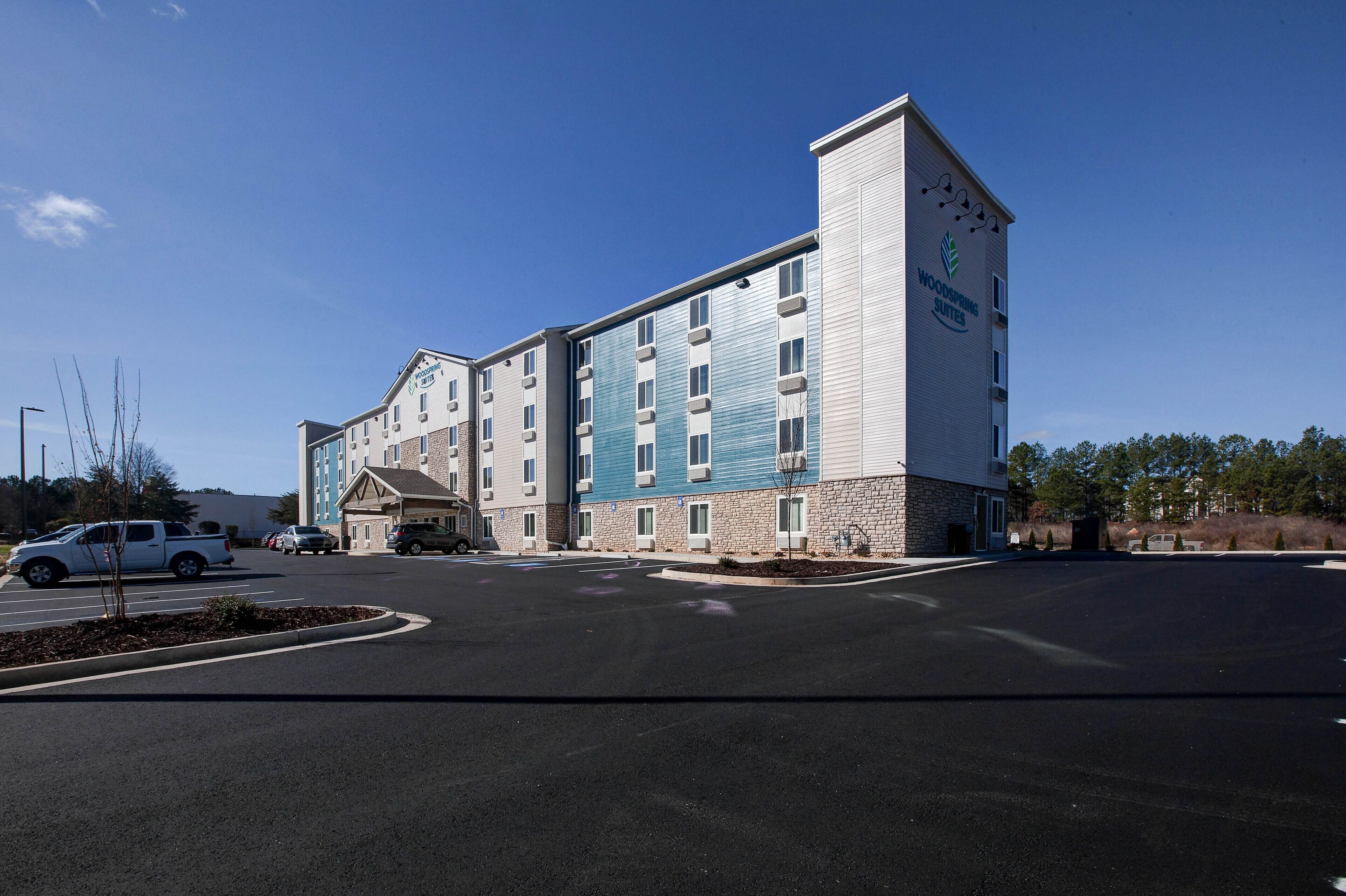 Un hotel de varios pisos con fachada de piedra y detalles azules, que cuenta con un estacionamiento y un cielo despejado.
