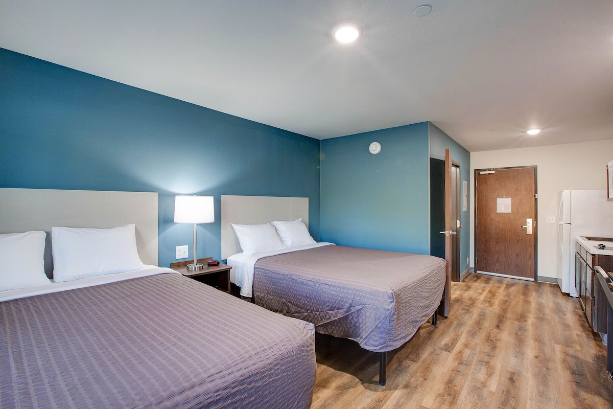 A hotel room with two beds, a nightstand, a desk, and a door leading to a bathroom.