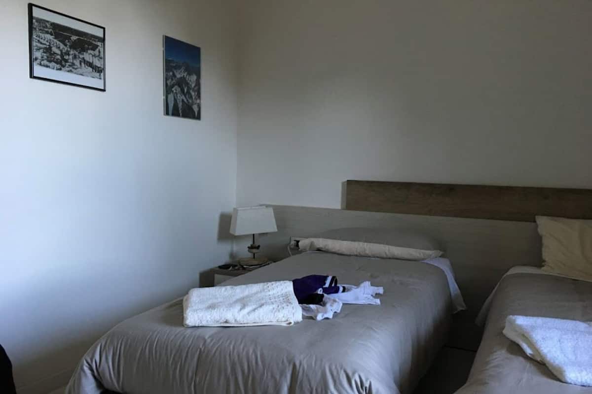 A hotel room with two beds, a wooden headboard, a nightstand with a lamp, and two framed pictures on the wall.