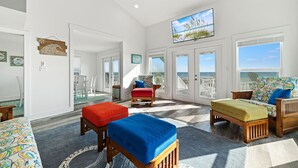 Un salon spacieux doté d’une grande fenêtre, d’un ventilateur de plafond et d’un téléviseur fixé au mur.