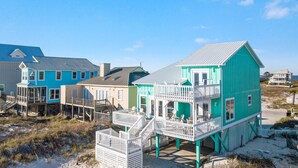 Une propriété située en bord de mer, comprenant plusieurs bâtiments, dont une maison turquoise remarquable avec un balcon et une clôture blanche.