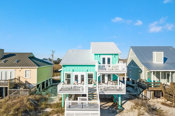 A beachfront property with multiple houses featuring balconies and a sandy beach area. - Recently updated, beautifully furnished gulf front home with decks galore! (Gulf Shores)