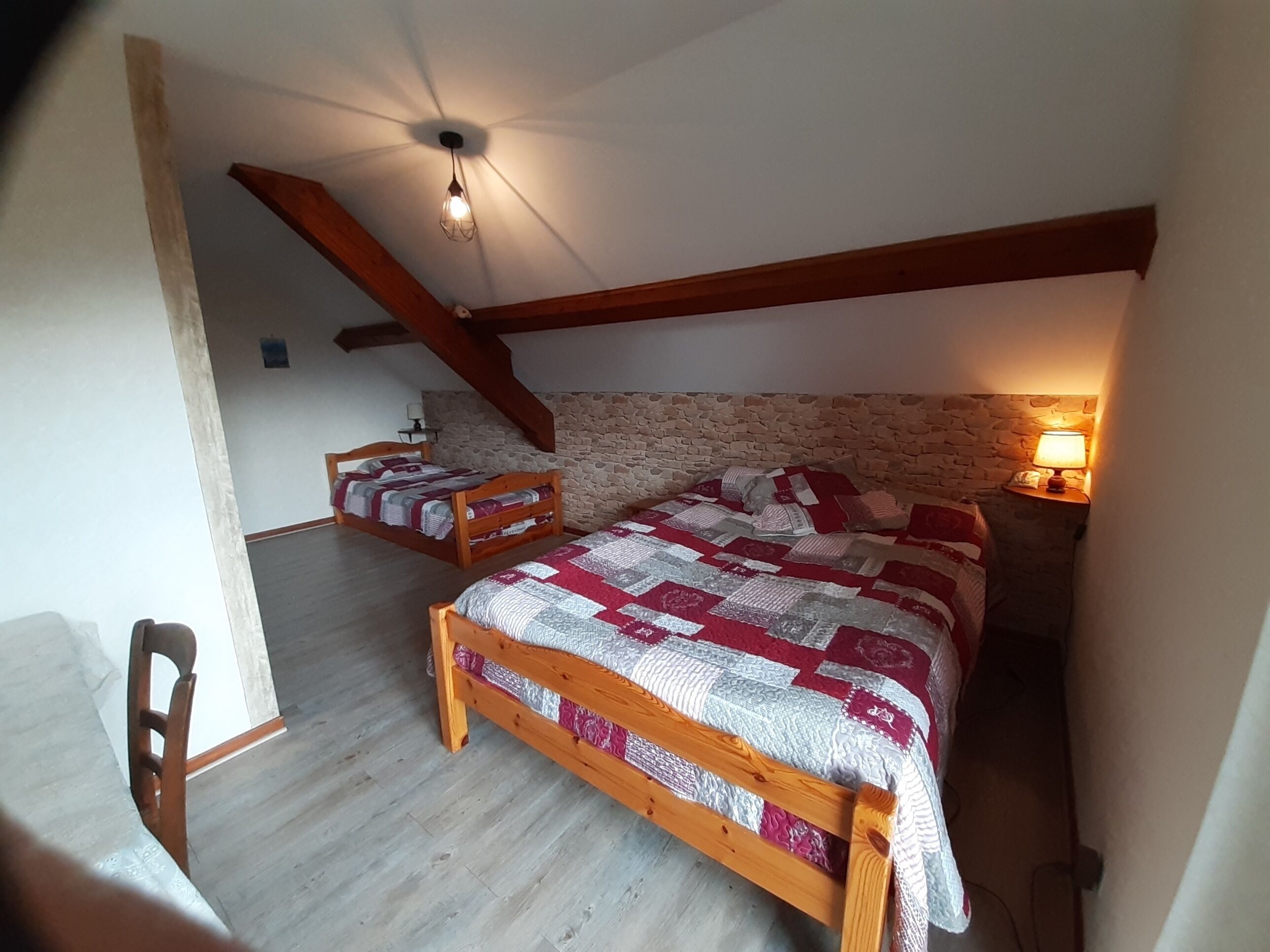 A bedroom with a sloped ceiling, a wooden bed, a stone wall, and a nightstand with a lamp.
