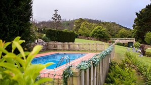 A swimming pool surrounded by a wooden fence, with a grassy area and trees in the background. - TWO ROOM APARTMENT (Laxe)