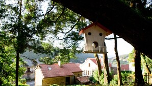 A rustic birdhouse hanging from a tree in a lush, green landscape with houses in the background. - TWO ROOM APARTMENT (Laxe)