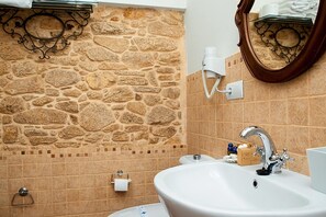 A bathroom with a stone wall, a white sink, a mirror, and a hairdryer on the wall. - TWO ROOM APARTMENT (Laxe)