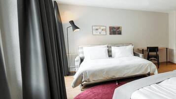 A hotel room with a bed, a desk, a chair, a lamp, and a radiator.