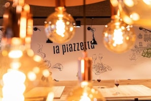 A restaurant interior with hanging light bulbs, a wall with sketches, and a table with a wine glass. - Hotel Stockalperhof (Brig)