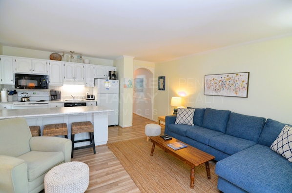 A compact living space with a kitchenette, a blue sofa, a coffee table, and a small dining area.