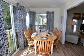 A dining area with a round table, six wooden chairs, and a glass door leading outside.