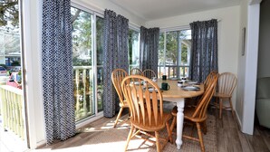 Un coin repas avec une table et des chaises en bois, des rideaux à motifs et de grandes fenêtres.