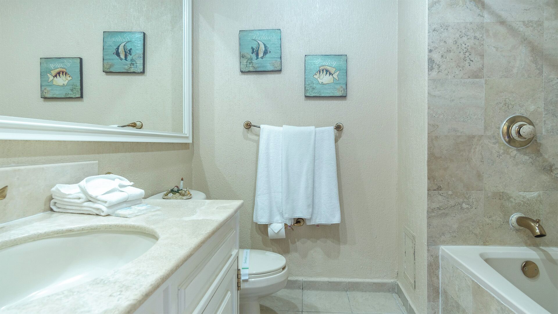 Une salle de bain avec une baignoire, des toilettes et un lavabo. Trois tableaux représentant des poissons sont accrochés au mur.