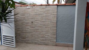 Un muro de piedra con una reja metálica, un respiradero blanco y una pared azul con textura.