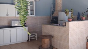 Una cocina con armarios blancos, un microondas y un taburete de madera. Hay plantas en macetas sobre la encimera y una escalera apoyada en la pared.