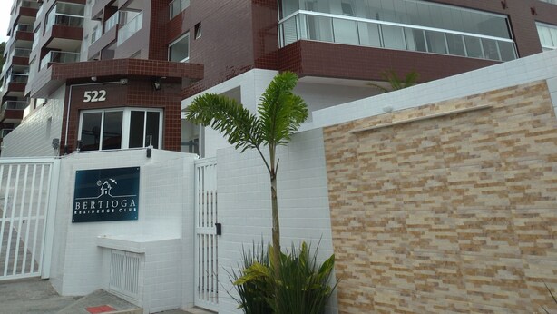 Un edificio residencial de varios pisos con un diseño moderno, que destaca por una entrada con el letrero 'Bertioga Residence Club'.