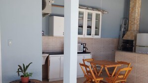 Una cocina con armarios blancos, microondas y cafetera. Hay una mesa redonda de madera con sillas y una planta en maceta.