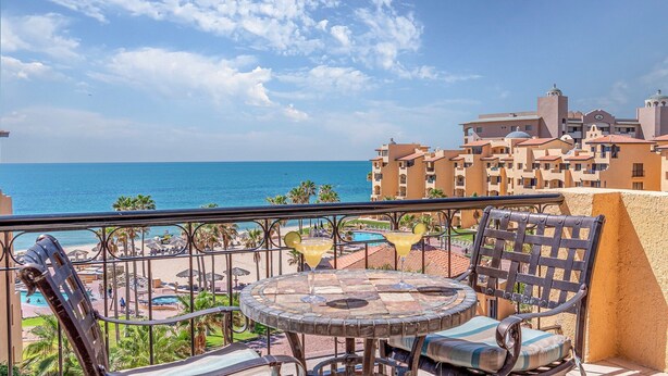 Un balcon avec vue sur la mer, un espace piscine et une table à manger avec des chaises.