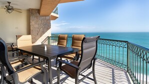 A balcony with a table and chairs, a ceiling fan, and a view of the sea.