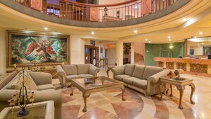 A spacious lobby with a high ceiling, a grand staircase, and a reception desk.