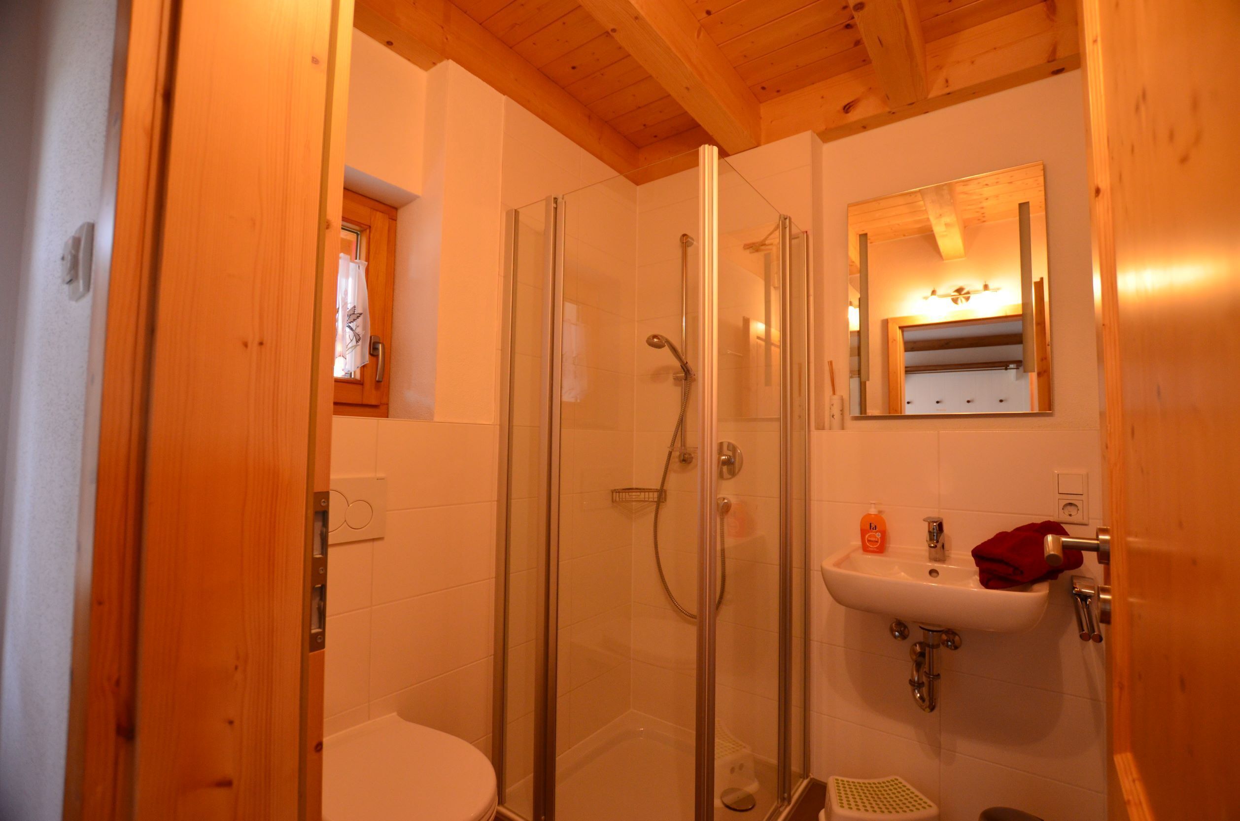 A wooden-paneled bathroom with a glass-enclosed shower, a white sink, and a small window above the toilet.