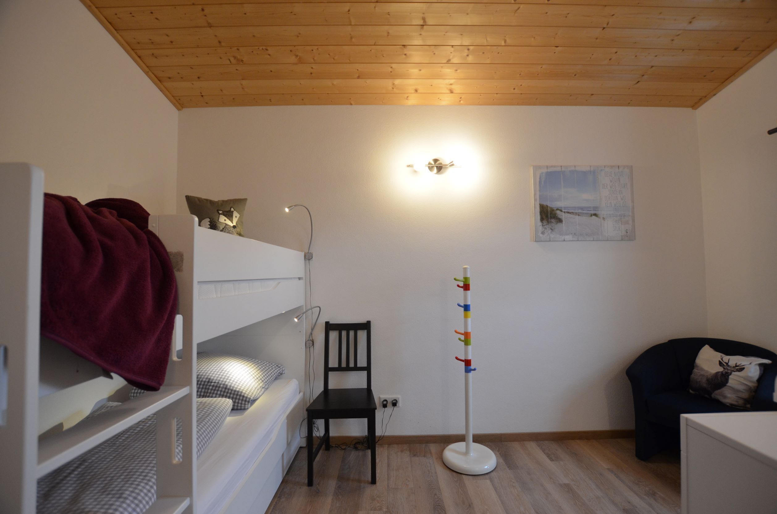 A room with bunk beds, a chair, a coat rack, and a painting on the wall.