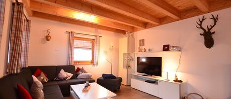 A modern living room with a wooden ceiling, a grey sofa, a white coffee table, a flat-screen TV, and a mounted deer head on the wall.