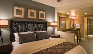 Une chambre d’hôtel dotée d’un grand lit, de deux lampes de chevet, d’une tête de lit au design original, d’une salle de bain avec une douche en verre et d’œuvres d’art encadrées accrochées au mur.