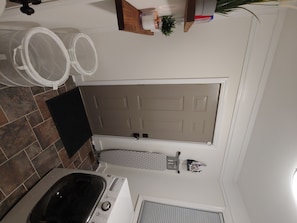 A bathroom with a bathtub, a toilet, and a shower. There is a towel rack above the shower and a small potted plant on the wall.