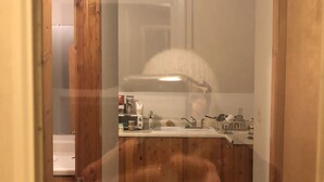 Ein schmaler Flur führt zu einer Küche mit Holzschränken, einem Spülbecken und diversen Küchenutensilien.