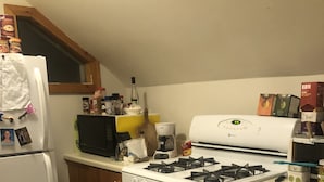 Eine Küche mit einem weißen Kühlschrank, Herd und Backofen. Es gibt Schränke, eine Mikrowelle und verschiedene Küchenutensilien auf der Arbeitsfläche.