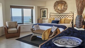 A bedroom with a large bed, a chair, a view of the sea, and a decorative wall piece. - Beach front 2 Bedroom 2 Bathroom luxury condo with amazing views.  (Cabo San Lucas)