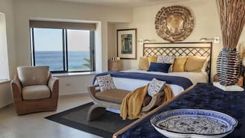A bedroom with a large bed, a chair, a view of the sea, and a decorative wall piece.