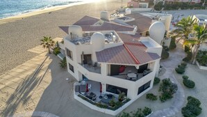 A multi-story building with a rooftop terrace, adjacent to a sandy beach. - Beach front 2 Bedroom 2 Bathroom luxury condo with amazing views.  (Cabo San Lucas)