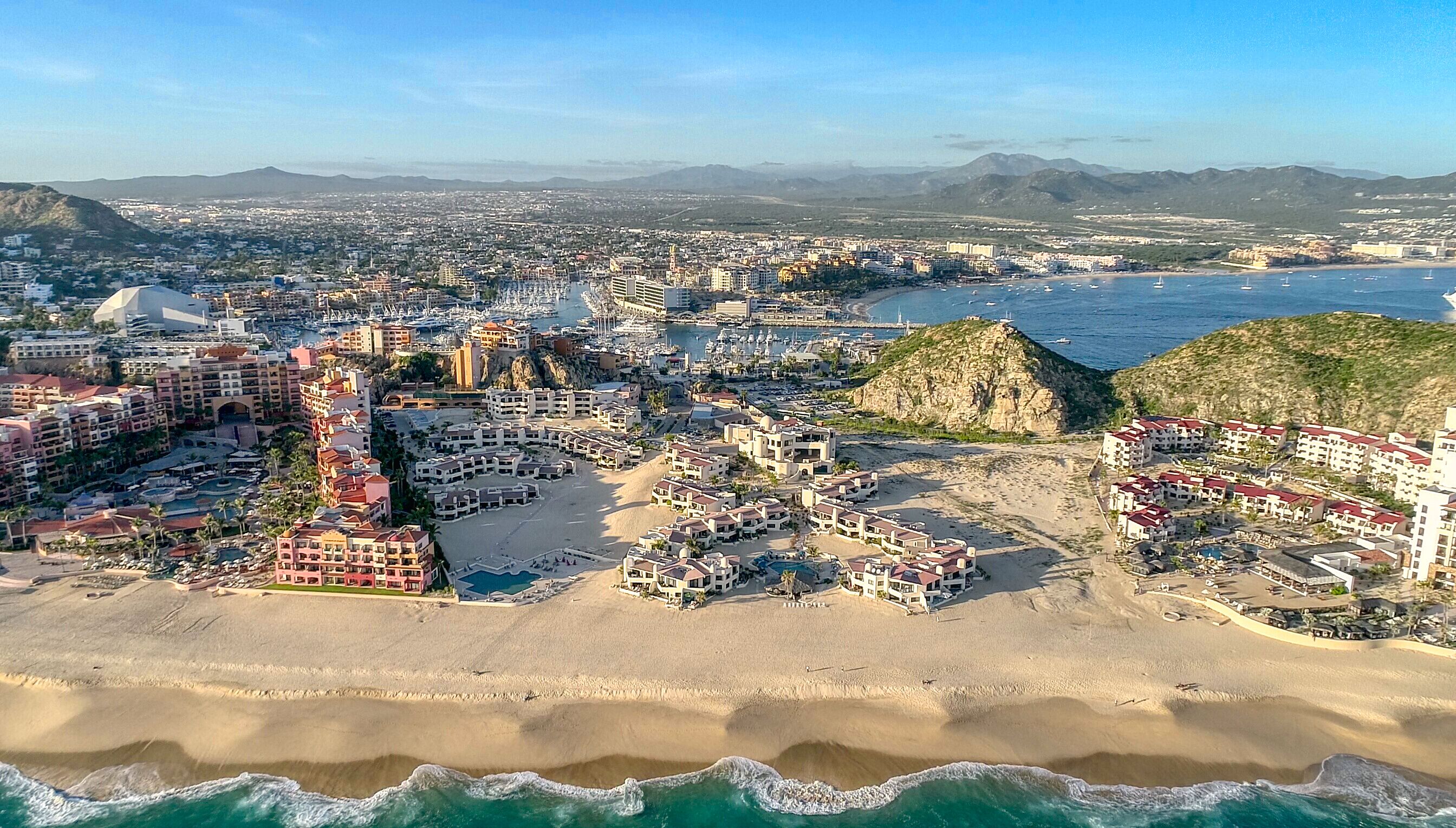 An aerial view of a coastal city with a prominent beach, hotels, and a rocky outcrop.