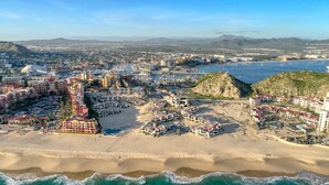 An aerial view of a coastal city with a prominent beach, hotels, and a rocky outcrop. - Beach front 2 Bedroom 2 Bathroom luxury condo with amazing views.  (Cabo San Lucas)