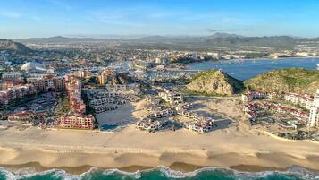An aerial view of a coastal city with a prominent beach, hotels, and a rocky outcrop.