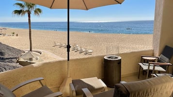 A balcony with a view of the beach, lounge chairs, and a trash can.