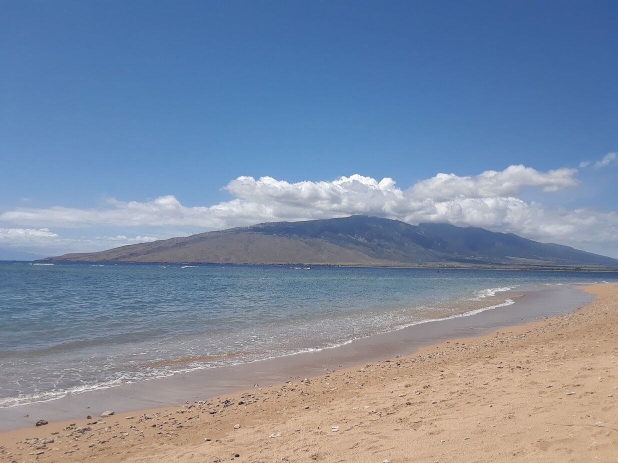Une plage à l’eau claire, un rivage sablonneux et une montagne en arrière-plan.