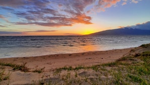 Une plage offrant une vue sur le coucher de soleil, avec un rivage sablonneux et des dunes herbeuses.