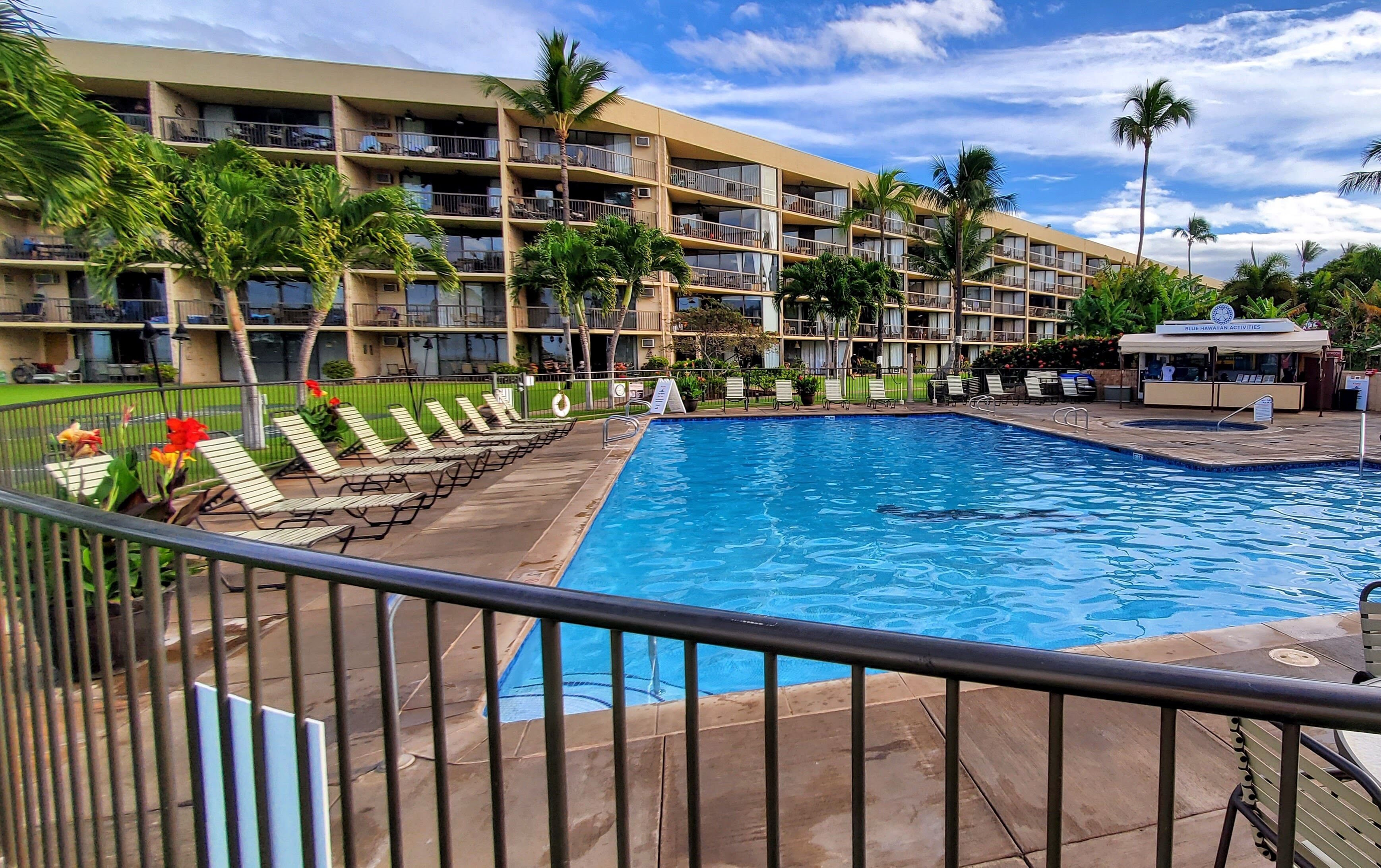A hotel with a swimming pool, multiple balconies, and palm trees.