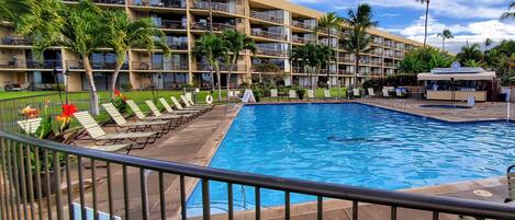 A hotel with a swimming pool, multiple balconies, and palm trees.
