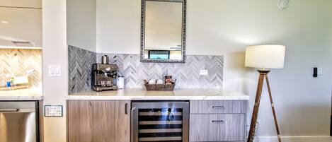 A modern kitchen with a coffee machine, a microwave, and a dishwasher. There is a mirror above the counter and a floor lamp to the right.