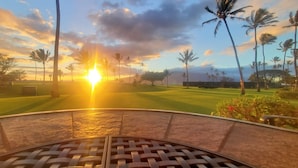 Un parcours de golf offrant une vue sur le coucher de soleil, avec des palmiers et un ciel dégagé.