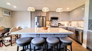 Une cuisine moderne dotée d’un grand îlot central, de tabourets de bar et de luminaires suspendus.