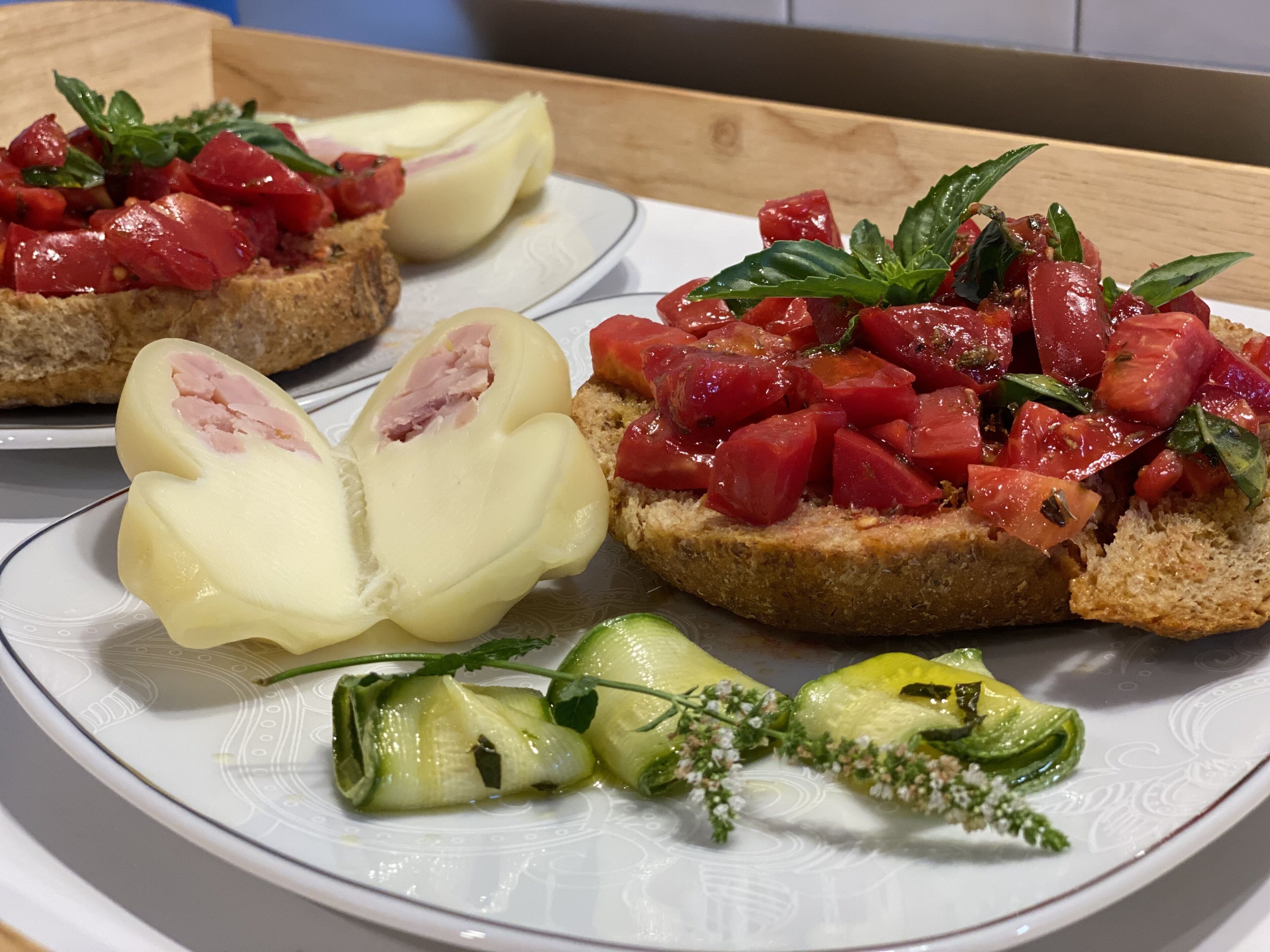A plate with bruschetta topped with tomatoes and mozzarella, accompanied by a side of sliced zucchini and herbs.