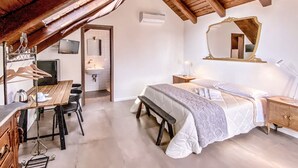 A bedroom with a wooden ceiling, a bed with a white and gray quilt, a bedside table with a lamp, a mirror, and a wooden bench. - Tenuta Novecento Bio Agriturismo (Agerola)