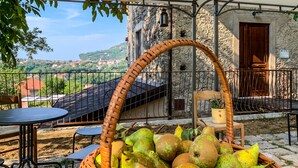 A wicker basket filled with pears on a patio with a stone wall and a view of a village in the background. - Tenuta Novecento Bio Agriturismo (Agerola)